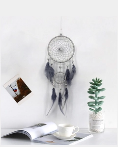 Gray double-ring dreamcatcher with soft feathers hanging against a minimalist white wall