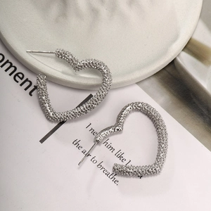 Silver heart hoop earrings with textured finish on a minimalist artistic background