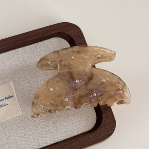 Detailed macro view of amber acetate hair claw clip with rhinestones on wooden tray