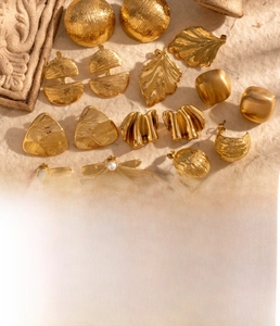 Détail de boucles d'oreilles en acier titane doré avec feuille de ginkgo et motifs
