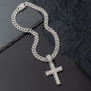 Close-up of silver Cuban chain necklace with sparkling iced out cross pendant on rock