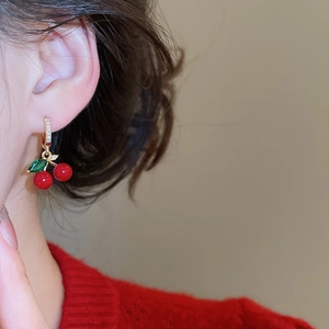 Close-up of cherry drop earrings with red stones and zircon leaves on a model's ear