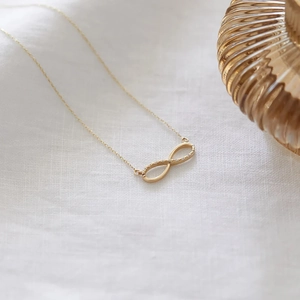 Infinity symbol necklace in gold with micro-set zircons on elegant white linen texture
