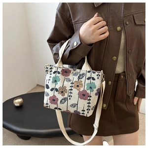 Detail of floral patterned beige fabric handbag with adjustable shoulder strap and short handles
