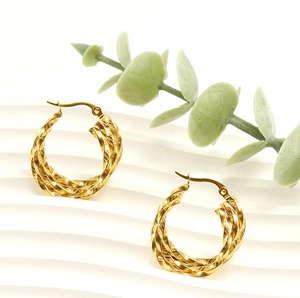Detail of gold twisted hoop earrings with textured finish on a white wavy background