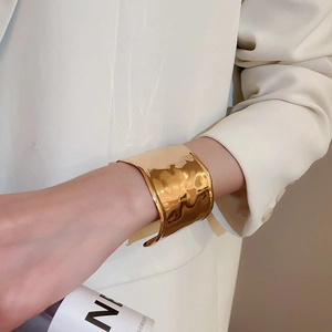 Close-up of golden wide cuff bracelet with a textured liquid metal finish on a white sleeve