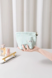 Blue and white striped makeup bag held by hand featuring a gold flower zipper puller