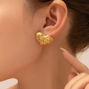 Close-up of gold heart-shaped stud earring with textured stripes on model ear
