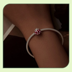 Close-up of a silver mesh bracelet featuring a red ladybug charm with pink dots on wrist