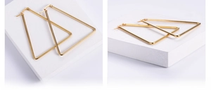 Detailed close-up of large golden geometric triangle earrings on white textured stone