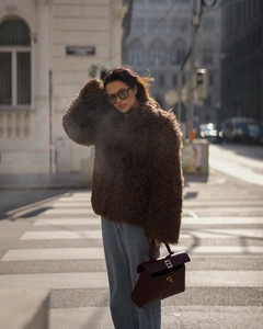 Street style shot of a plush dark brown faux fur jacket with a burgundy leather handbag