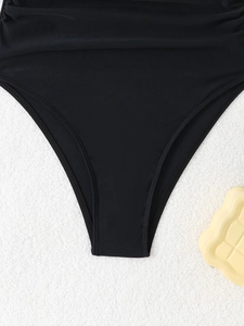 Detail showing high-cut leg opening and waist pleat design on black swimsuit fabric