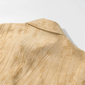 Detailed view of jacquard floral patterns and vertical pleats on gold satin shirt fabric