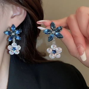Detail view of flower-shaped earrings with blue and white zircons on a model