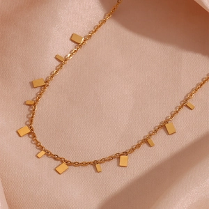 Detailed macro view of 18K gold plated square pendants on a thin chain over pink silk