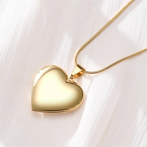 Detailed view of heart-shaped gold locket pendant with snake chain on white fabric