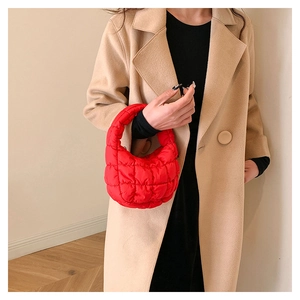 Detail of red quilted cloud bag with glossy nylon finish held against a beige coat