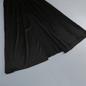 Detailed view of the black satin gown featuring a side slit and elegant draped hemline