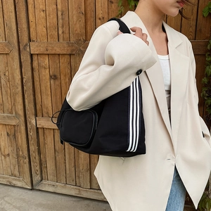 Minimalist black nylon shoulder bag with three white stripes and a small round coin pouch