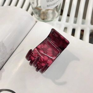 Gros plan d'une pince à cheveux marbrée rouge foncé avec finition brillante sur blanc