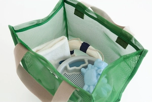 Detailed view of green mesh beach bag packed with towels and toys on white background