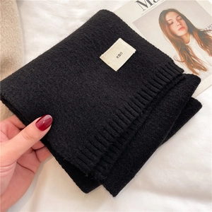 Close-up of black knitted scarf fabric and 'emo' label held by a hand on a bed