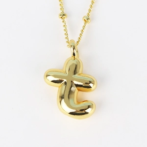 Detail of gold bubble letter t pendant with beaded chain on white background
