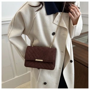 Detail of dark brown chevron quilted suede crossbody bag with gold chain strap on model