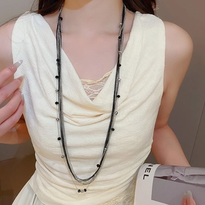 Detail view of multilayered long necklace with black beads and silver chain on model