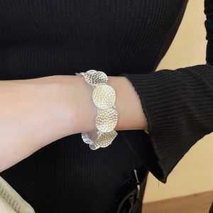 Detail showing the hammered texture of silver metallic disks on a worn elastic bracelet