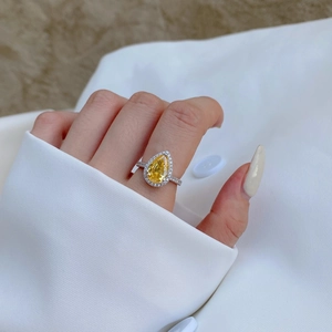 Macro shot of pear-cut yellow gemstone ring with pavé diamond halo on hand