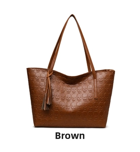 Detail of brown tote bag featuring embossed skull patterns and stylish leather tassel charm