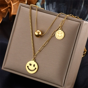 Détail du collier double couche doré avec chaîne serpent et pendentif visage souriant