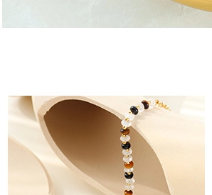 Detail of beaded bracelet with tiger eye and gold clasp on minimalist ceramic stand