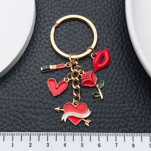 Golden keychain with red enamel lipstick, rose and heart charms on black leather background