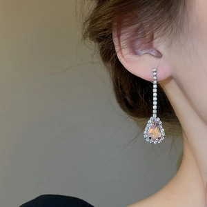 Close-up of pink teardrop earrings with crystals worn by a model in soft lighting
