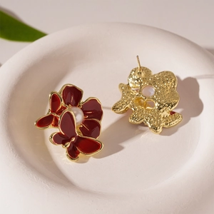 Macro detail of red enamel floral butterfly earrings with pearl on a white ceramic plate