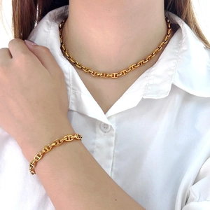Detail of golden pig nose link necklace and bracelet set worn on a white shirt