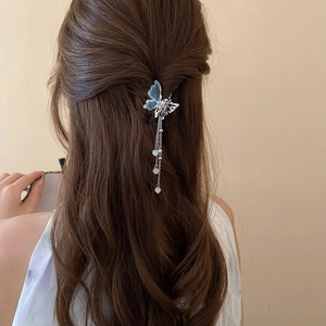 Détail d'une pince papillon bleue translucide avec glands perlés sur cheveux bouclés