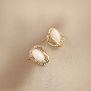 Elegant gold cat eye stone stud earrings with small crystal accents on beige silk