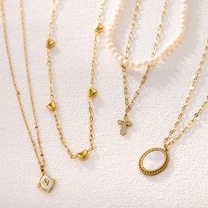 Layered gold necklaces with heart, cross, pearl and mother-of-pearl charms on white background
