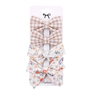 Detail of four fabric bow hair clips with brown plaid and floral patterns on card