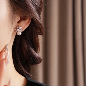 Close-up of pearl and zircon flower stud earrings worn by a model in soft lighting