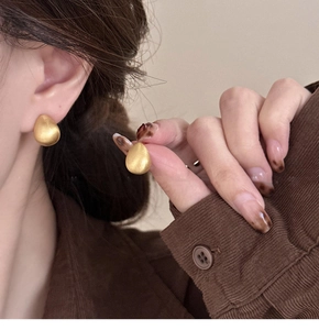 Detail view of 18k gold plated brushed teardrop earrings worn by a model in soft light