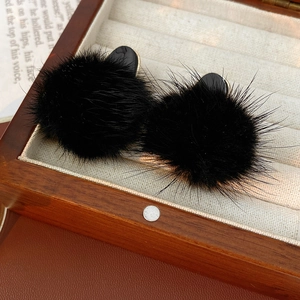 Macro detail of plush black pompom earrings with gold accents in a premium jewelry box