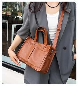Brown leather tote bag detail with large front pockets and adjustable shoulder strap