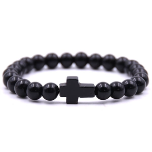 Detailed view of a black beaded bracelet featuring a minimalist cross pendant on white background