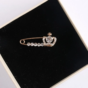 Close-up of golden crown brooch with sparkling rhinestones on black velvet cushion