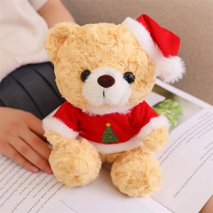 Close-up of a brown curly teddy bear in a red Christmas tree outfit reading a book