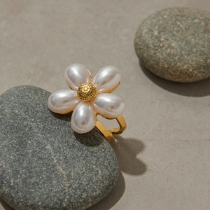 Detail of elegant gold flower ring with pearl petals on a natural gray stone background